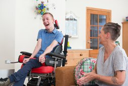 Eine Betreuerin und ein Mann im Rollstuhl lachen gemeinsam | © KIVILCIM - funky data - Getty Images